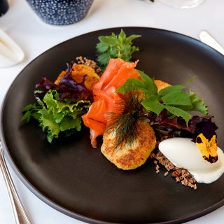 Romantik Hotel Hirschen: Gastgeber & Werte Gourmetgericht mit Lachs, grünem Salat und Creme auf schwarzem Teller