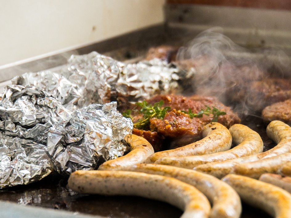 Services and rates for conferences and celebrations Sausages, meat, and foil on a hot grill with steam rising