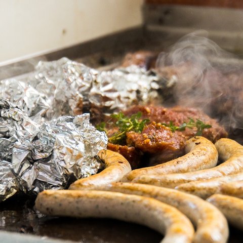 Beer garden in Parsberg: HirschenBlobb Sausages, meat, and foil on a hot grill with steam rising