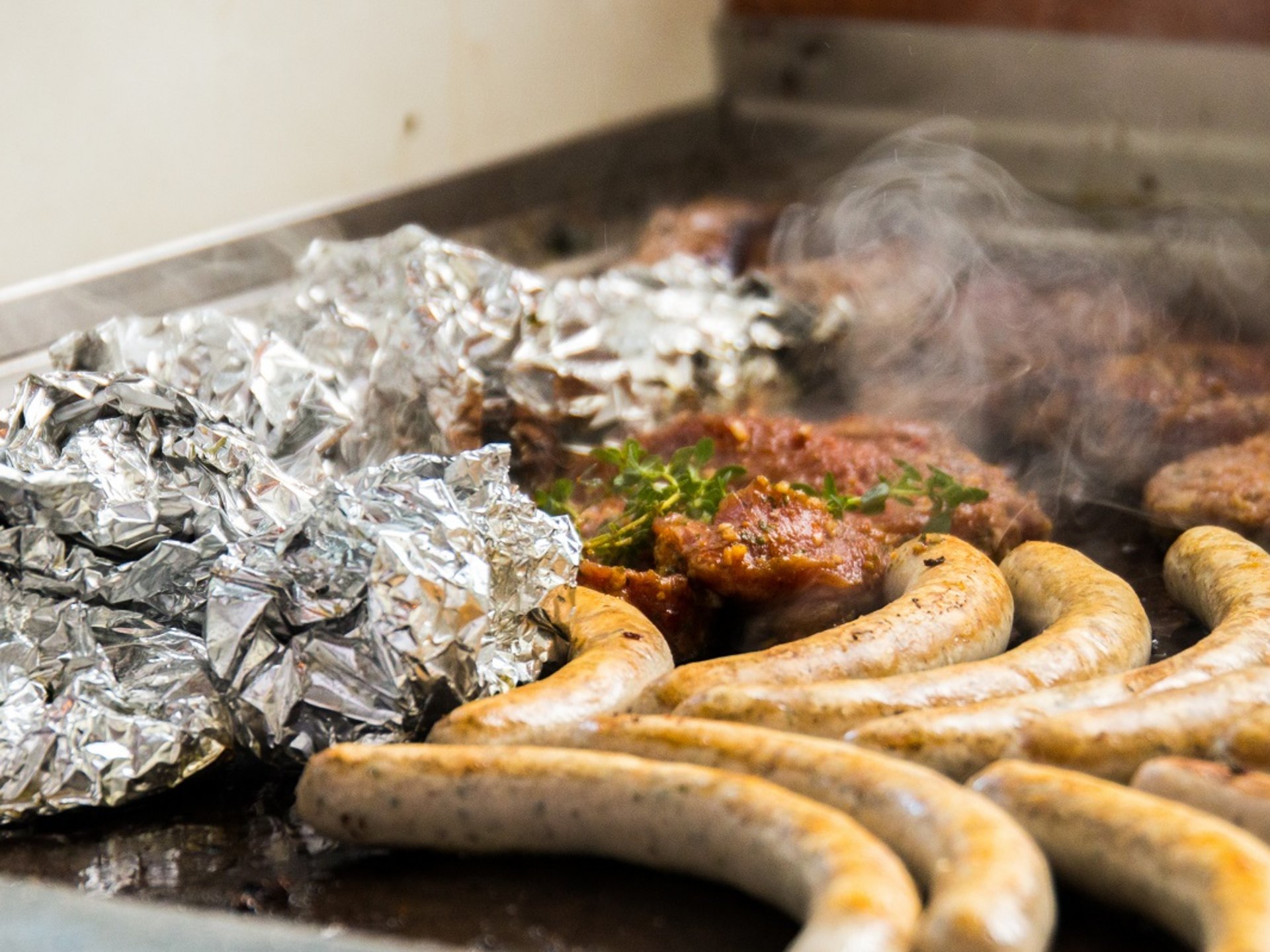 Teambuilding, Firmenevents & Rahmenprogramme Bratwürste, Alufolie und Fleisch auf einem heißen Grill mit Dampf