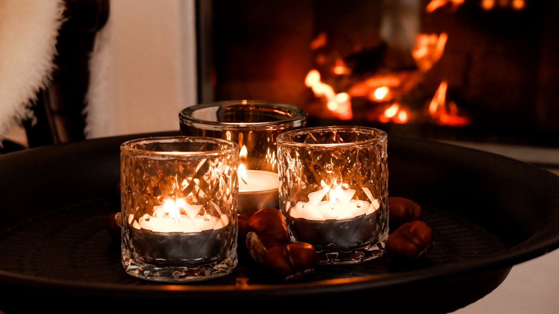 Weihnachtsmenüs 2025 Brennende Kerzen in Gläsern vor einem gemütlichen Kamin