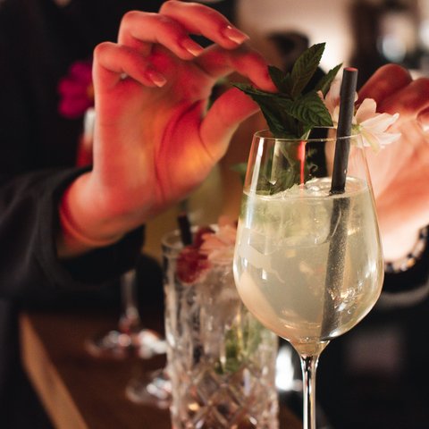 Hirschenblobb: unsere Bar Person dekoriert einen Cocktail mit Minzblättern und Blume in einer Bar.