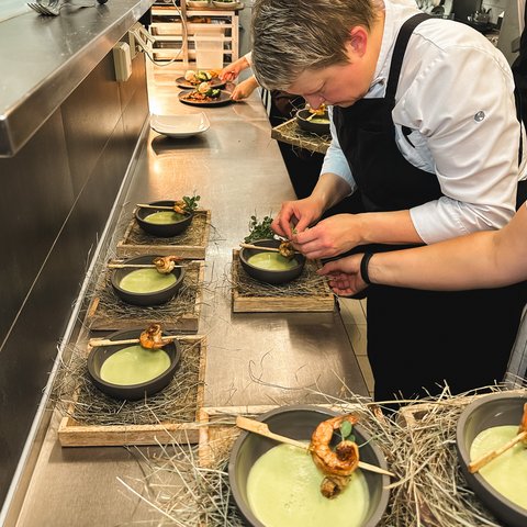 Restaurant in Parsberg: Gourmet genießen Köchin richtet Suppe mit Garnelen und grüner Beilage in einer Profiküche an