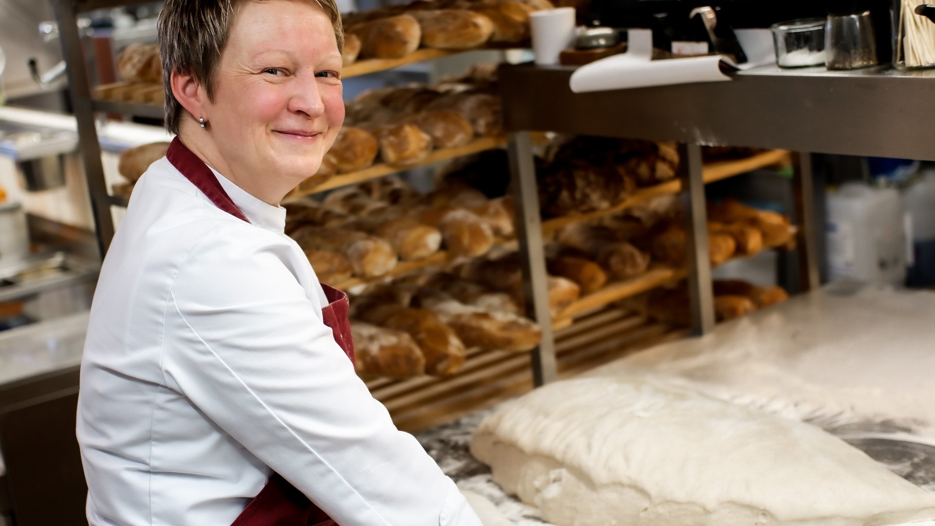 Bäckerin bereitet Teig in einer Backstube mit Brotregalen vor
