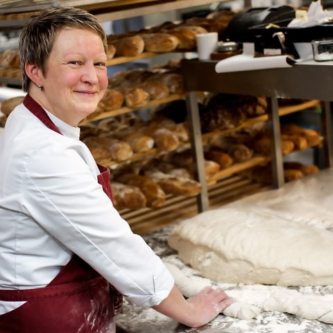 Eco-friendly hotel in Germany with Hirschenmanufaktur Baker preparing dough in bakery with shelves full of bread