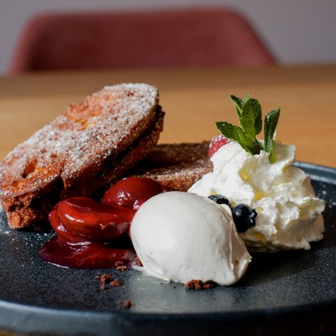 Kulinarik & Genuss in der Oberpfalz Dessert mit Kuchen, Vanilleeis, Kirschen und Sahne mit Minzblatt auf schwarzem Teller