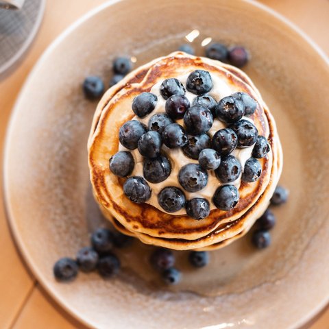 Brunch – breakfast for late risers Pancakes topped with blueberries and cream on a plate