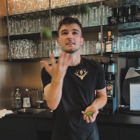 Hirschenblobb: Our bar Young man tossing limes behind bar with shelves full of glasses