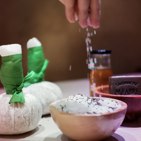Tageswellness in der Oberpfalz Hand streut Salz in Schale mit Kräutern, Spa-Accessoires im Hintergrund