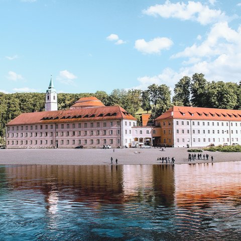 Romantik Hotel Hirschen: Gastgeber & Werte Kloster mit rotem Dach am Flussufer mit bewaldeten Klippen im Hintergrund