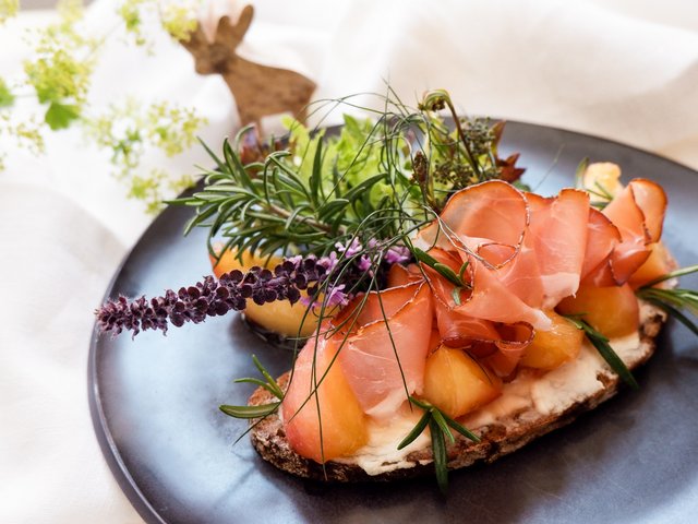 Romantik Hotel Hirschen: Bildergalerie Brot mit Schinken, Melone und frischen Kräutern auf einem schwarzen Teller
