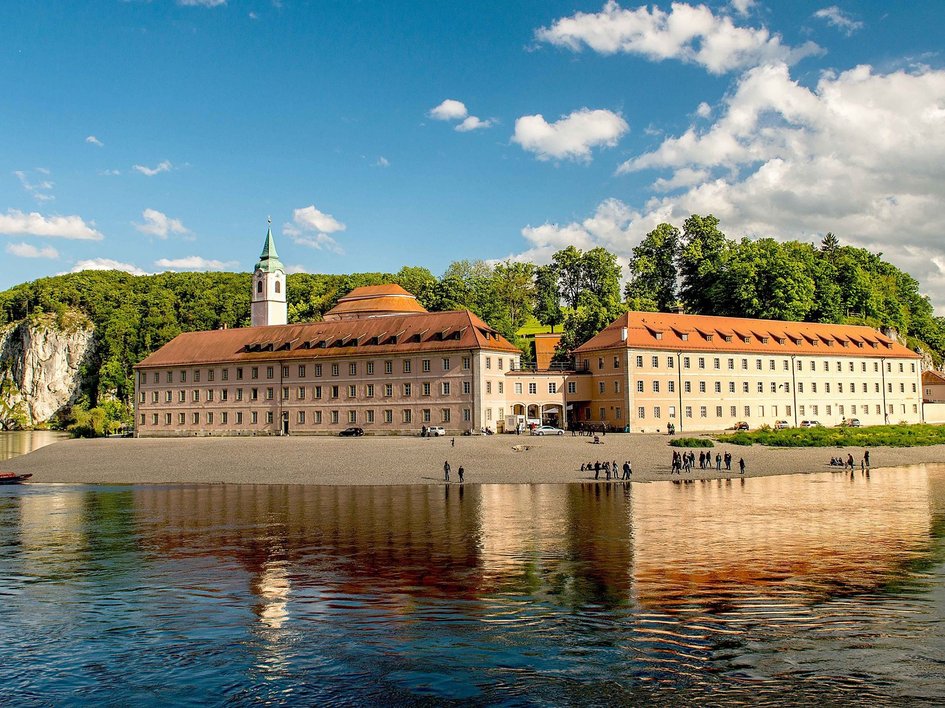 Hotels in Regensburg und Umgebung: kultur-trächtig! Kloster am Fluss mit Felsen und Bäumen unter blauem Himmel