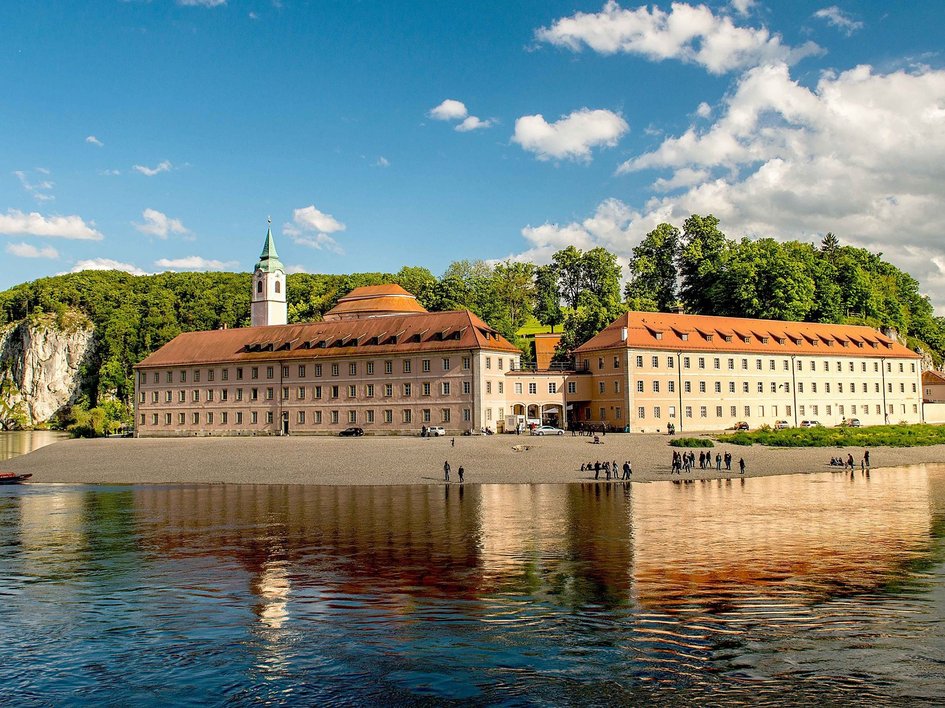 Hotels in Regensburg und Umgebung: kultur-trächtig! Kloster am Fluss mit Felsen und Bäumen unter blauem Himmel
