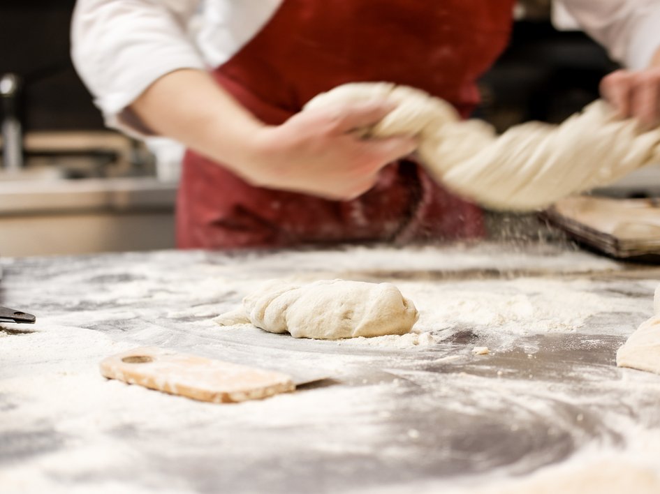 Nachhaltige Hotels in Deutschland gesucht? Bäcker knetet Teig auf bemehltem Tisch in Bäckerei