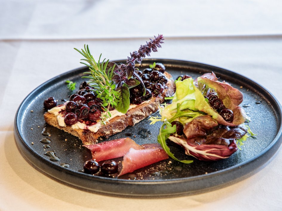 Hotel mit frühem Check-in Brot mit Frischkäse, Beeren, Salat und Schinken auf schwarzem Teller