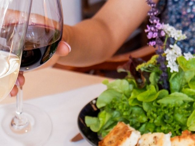 Romantik Hotel Hirschen: Bildergalerie Zwei Personen stoßen mit Rot- und Weißwein an bei feinem Essen im Restaurant