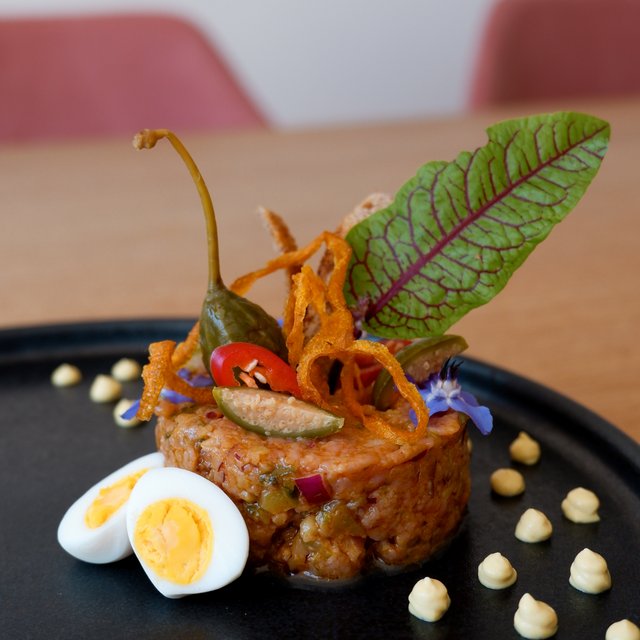 Romantik Hotel Hirschen: Kulinarik Fein angerichtetes Gericht mit Salatblatt, Wachtelei und Saucentropfen auf schwarzem Teller