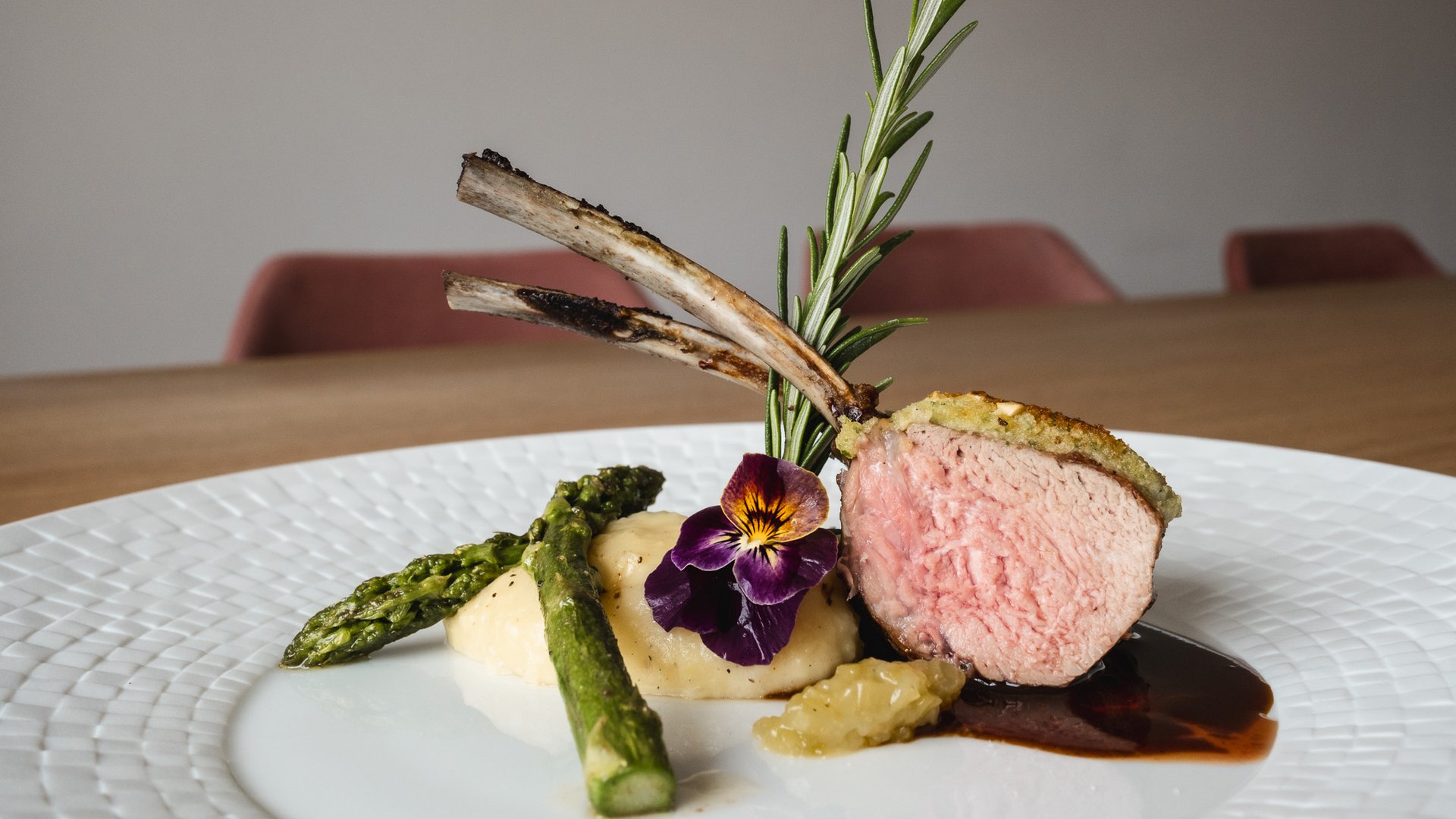 Restaurant in Parsberg: Gourmet genießen Lammkotelett mit Kräuterkruste, Spargel und Blumendekoration auf weißem Teller