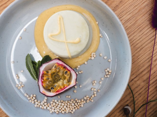 Romantik Hotel Hirschen: Bildergalerie Dessert mit Passionsfrucht, Minze und körnigem Belag auf grauem Teller