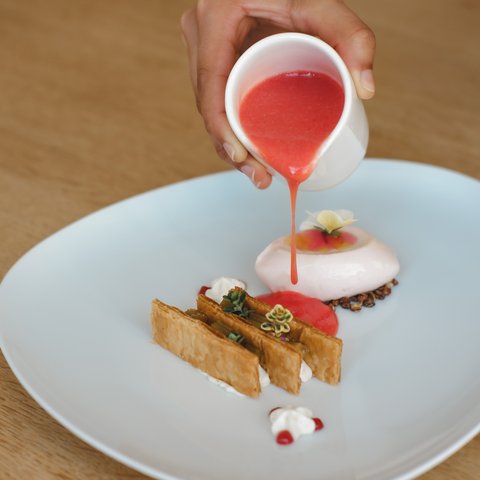 Restaurant in Parsberg: Gourmet genießen Hand gießt rote Sauce auf feines Dessert auf weißem Teller